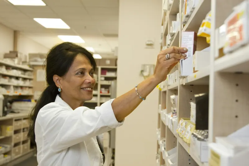 Farmacêutica de jaleco branco pegando um medicamento na prateleira